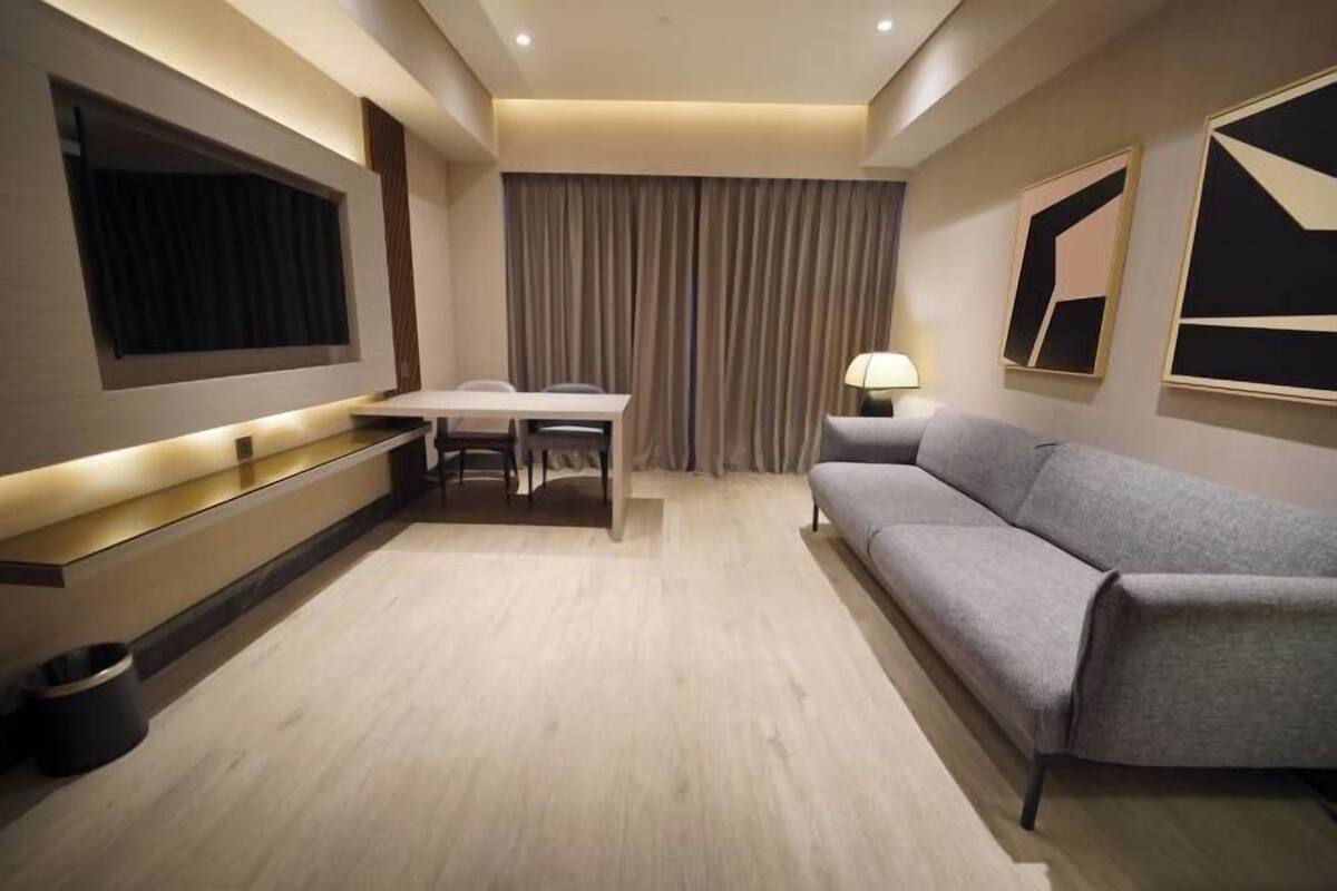 Ein modernes Hotelzimmer mit Flachbildfernseher, einer Sitzecke, einem Esstisch und einer Lampe.