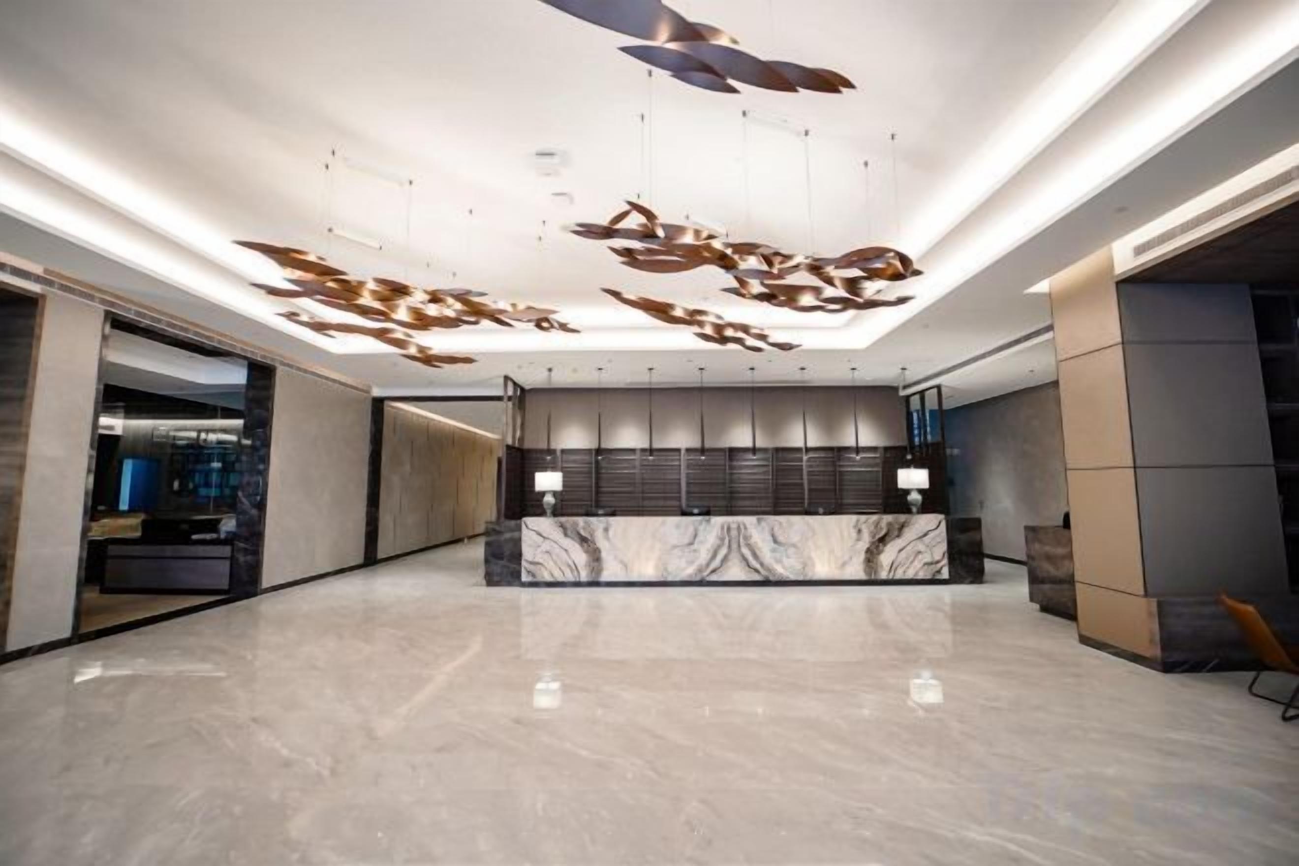 A spacious lobby with a marble reception desk, modern lighting, and a unique ceiling design.