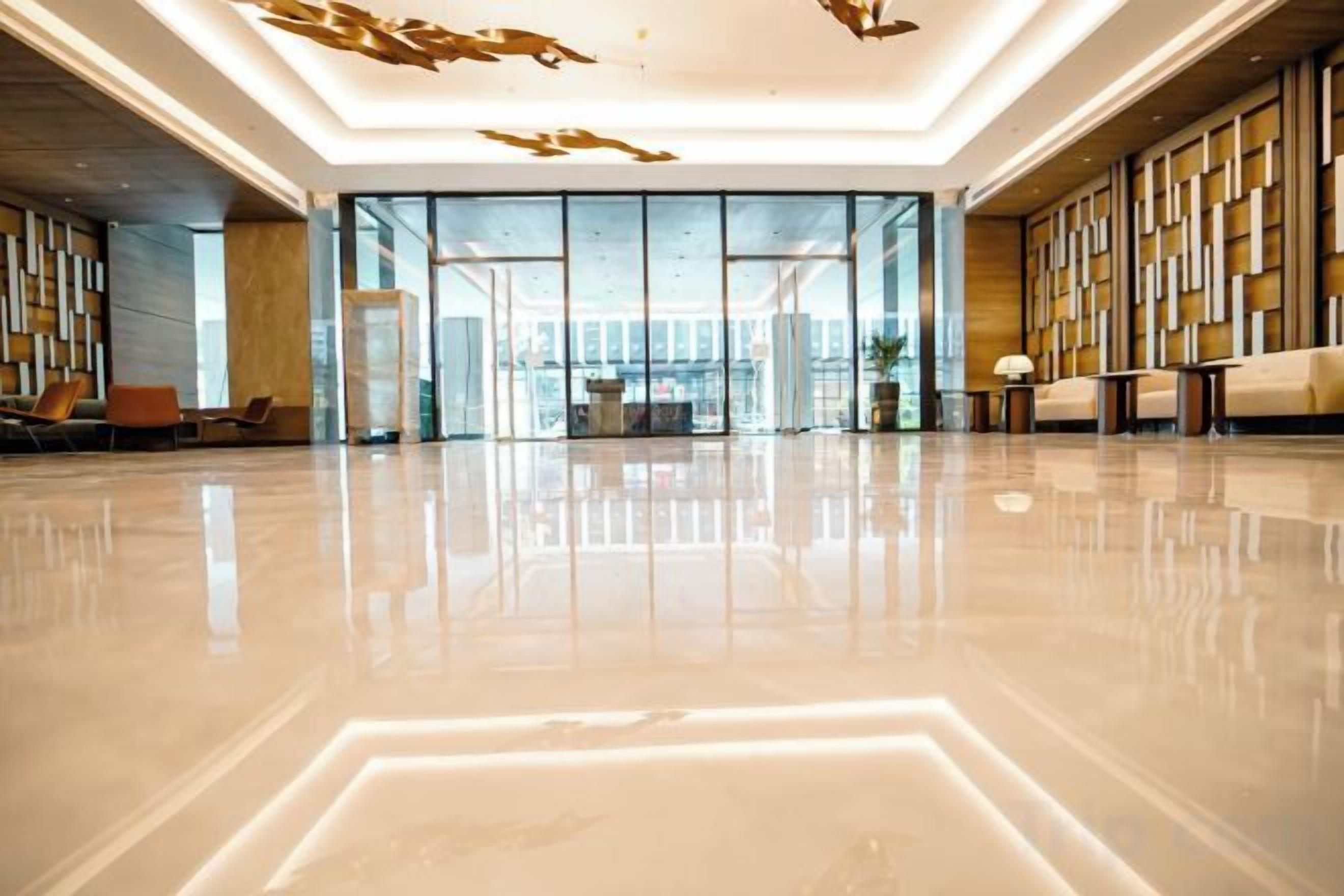 A spacious lobby with a reflective floor, seating areas, and a view through the glass doors.