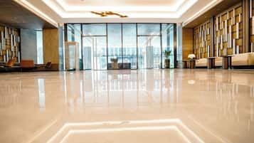 A spacious lobby with a reflective floor, seating areas, and a view through the glass doors.