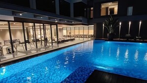 Une piscine intérieure moderne avec des murs en verre, un espace détente et un éclairage extérieur soigné.