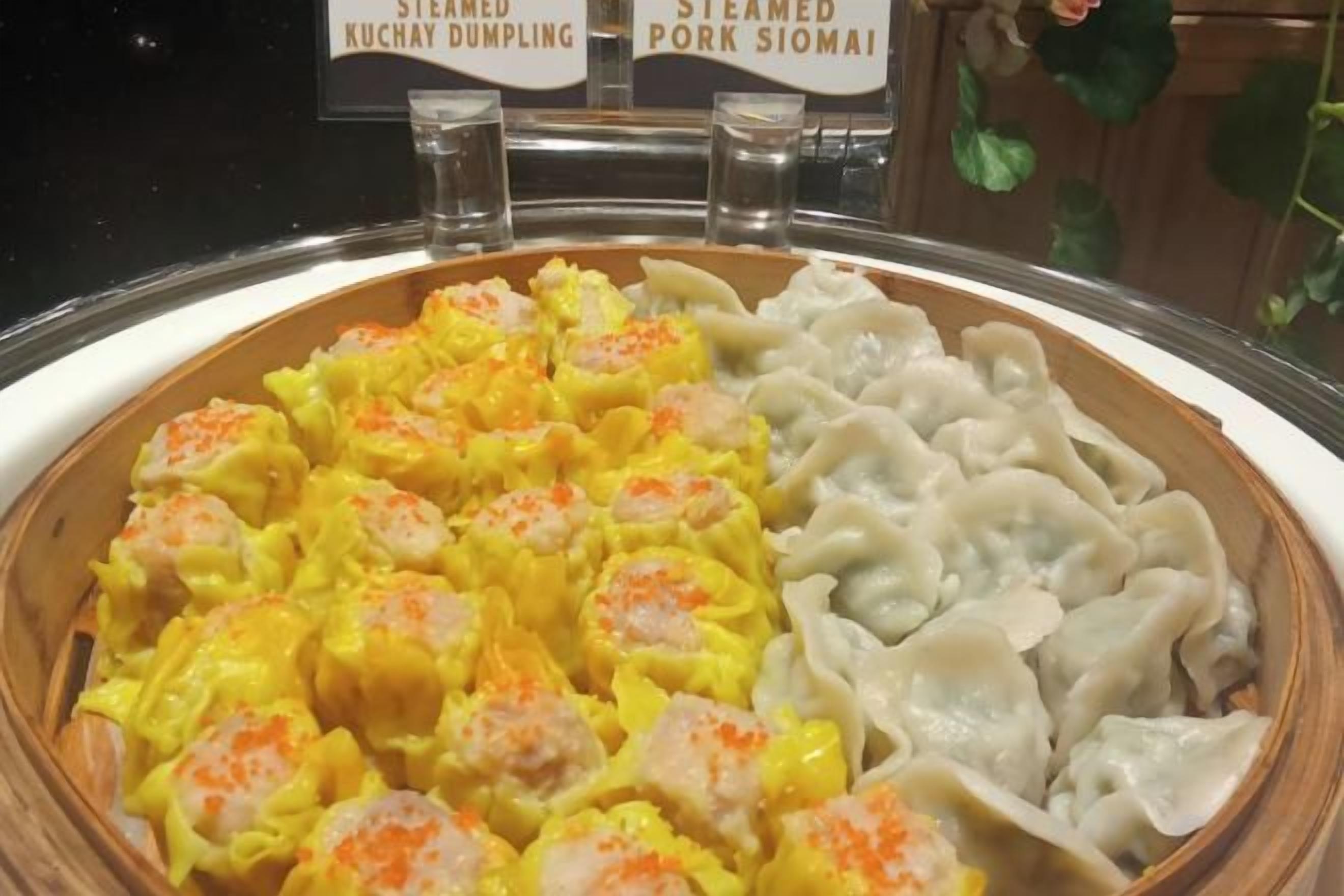 A buffet with steamed dumplings and a sign indicating the types of dumplings available.