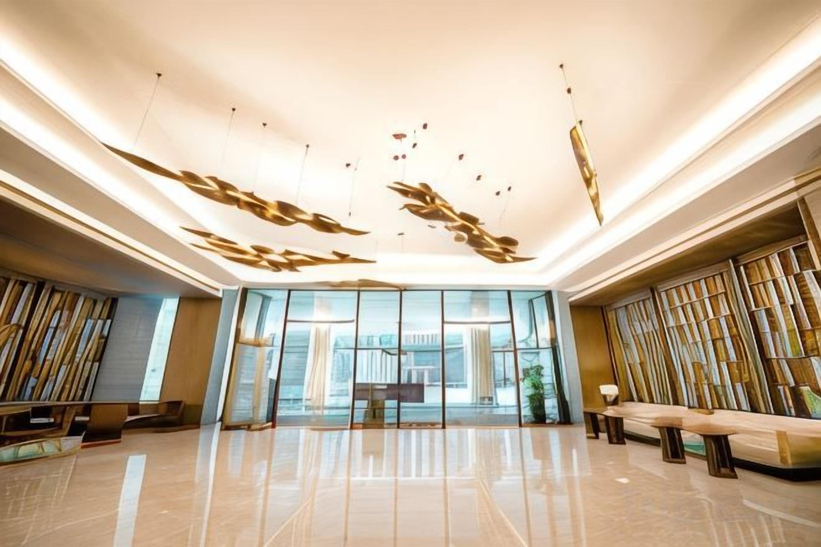 A spacious lobby with a modern design, featuring a seating area, a reception desk, and a large glass wall providing a view of the outdoors.