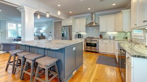 Una cocina amplia con una isla grande, armarios blancos, electrodomésticos de acero inoxidable y una lámpara colgante moderna.
