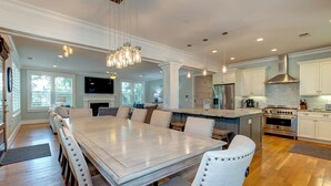 Un comedor amplio con una mesa larga y sillas, una cocina con electrodomésticos modernos, y un gran ventanal que proporciona luz natural.