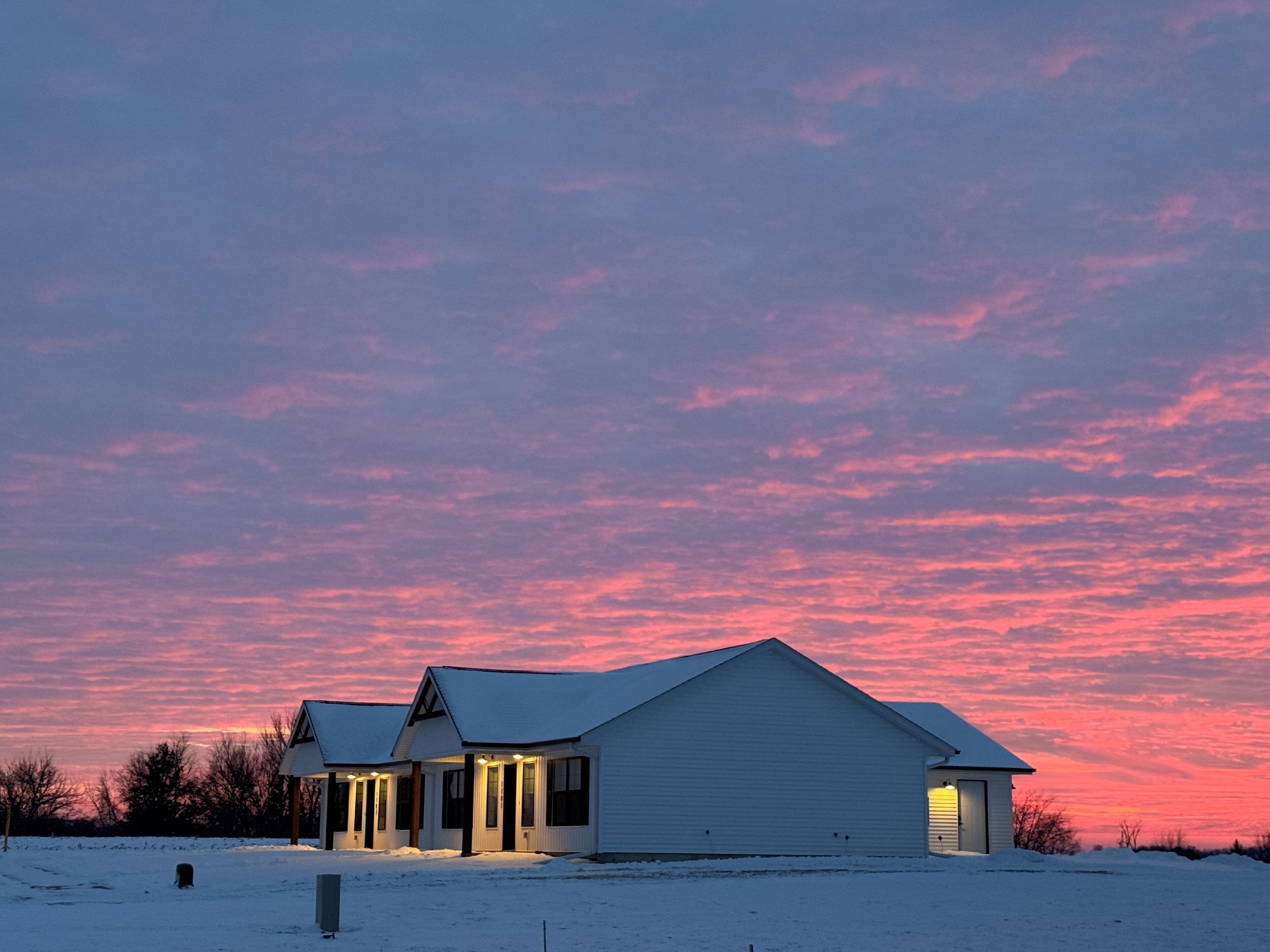 Una casa de dos pisos con un césped cubierto de nieve y un cielo rosado al anochecer.