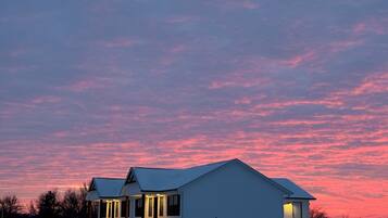 Una casa de dos pisos con un césped cubierto de nieve y un cielo rosado al anochecer.