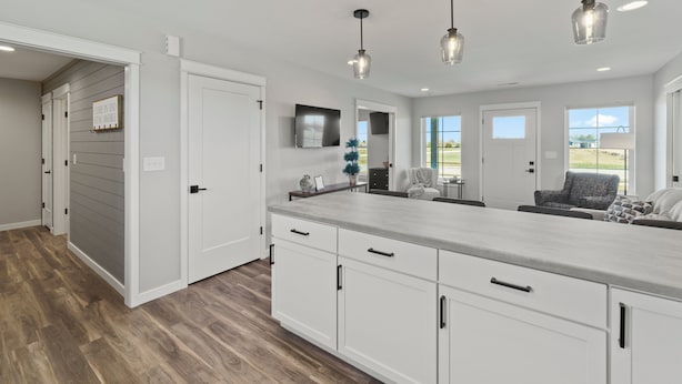 A modern kitchen with white cabinetry, a large island, pendant lighting, and a view of the outdoors through large windows. - Country Club Cottages - 1703 (Washington)