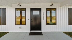 A white building with a black front door, numbered 1703, and two windows with dark frames. - Country Club Cottages - 1703 (Washington)