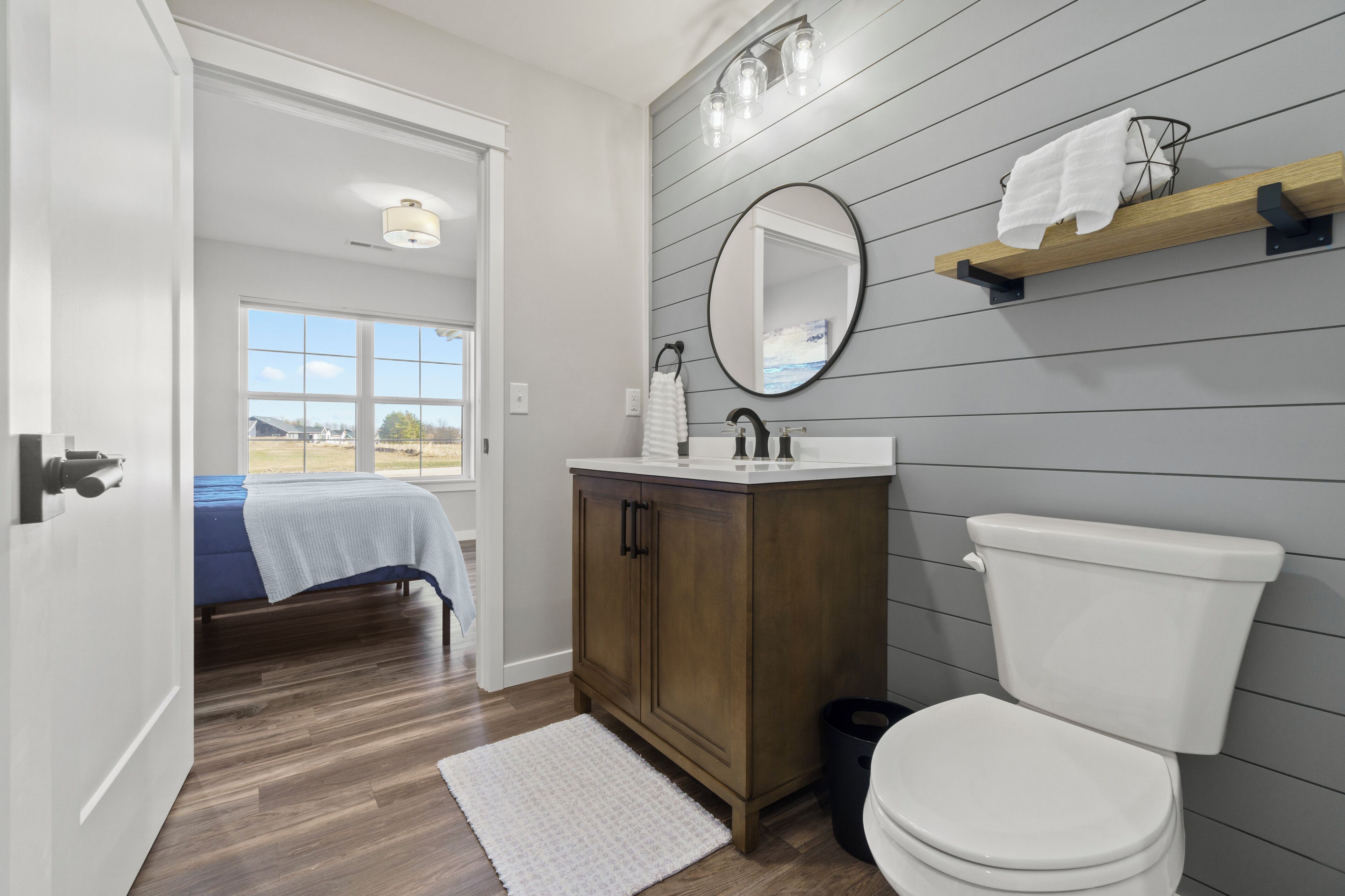 A bathroom with a wooden vanity, a white toilet, a large mirror, and a towel rack.