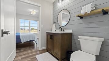 A bathroom with a wooden vanity, a white toilet, a large mirror, and a towel rack.