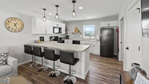 A modern kitchen with a central island, bar stools, and pendant lighting. - Country Club Cottages - 1703 (Washington)