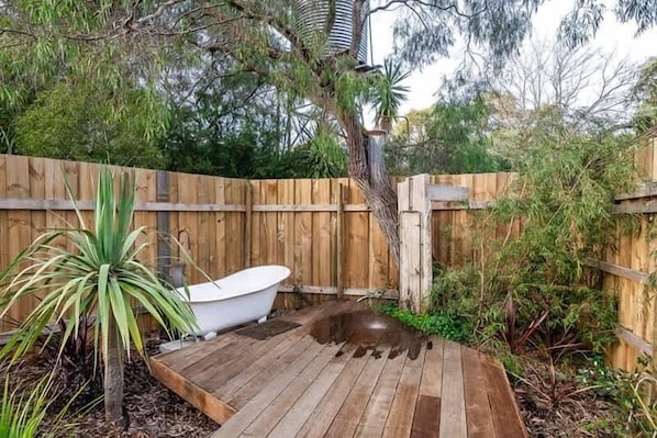 A wooden deck with a white bathtub, surrounded by a wooden fence and various plants.