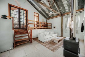 A spacious living area with a white sofa, wooden staircase, and a ceiling fan. - Orchard Cottage—Romantic Bushland Wellness Retreat (Yallingup Siding)
