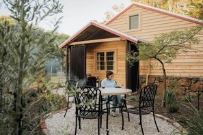 Une cabane en bois avec un porche couvert, une table ronde et des chaises.