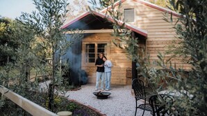 A wooden cabin with a red roof, a fire pit, and a patio area surrounded by plants. - Orchard Cottage—Romantic Bushland Wellness Retreat (Yallingup Siding)