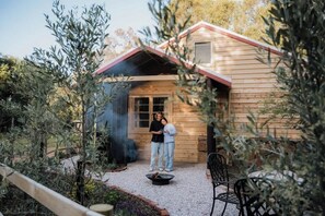 A wooden cabin with a red roof, a fire pit, and a patio area surrounded by plants. - Orchard Cottage—Romantic Bushland Wellness Retreat (Yallingup Siding)