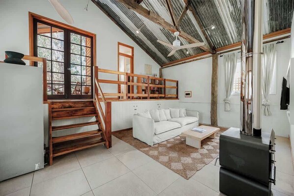 Ein geräumiger Wohnbereich mit einem weißen Sofa, einer Holztreppe und einem Deckenventilator.