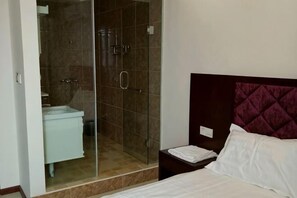 A bedroom with a bed, a nightstand, a marble-tiled shower enclosure, and a white sink. - Xiang Long Hotel (Guanghan)