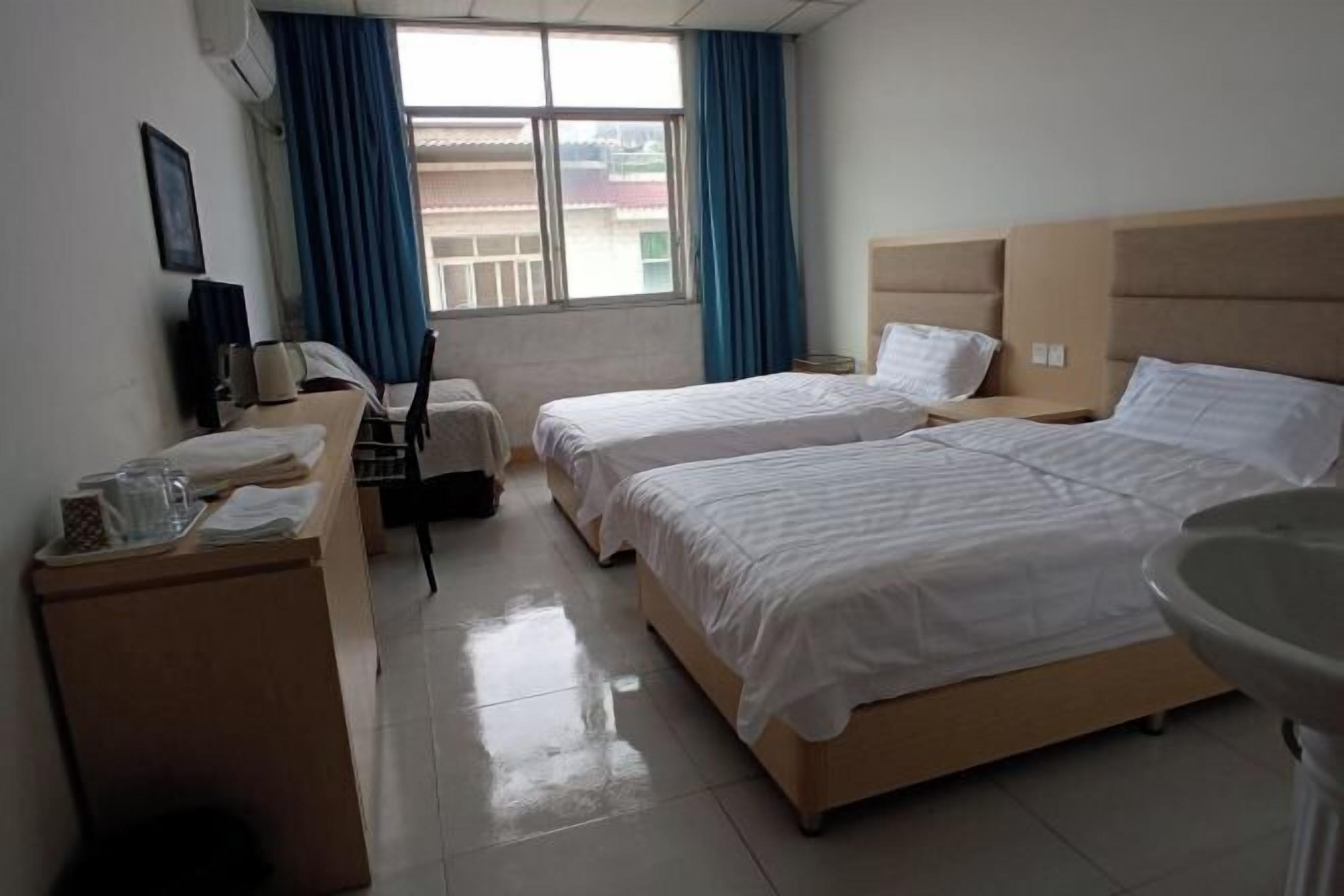 A hotel room with two beds, a desk, a chair, a TV, and a window with curtains.