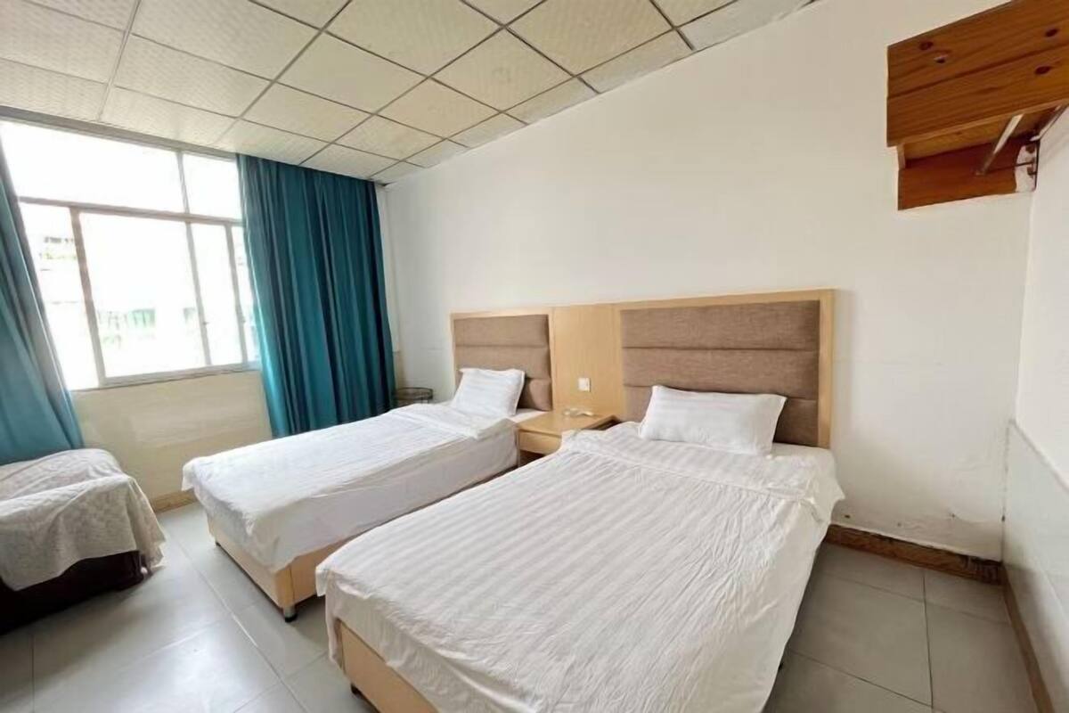 A hotel room with two single beds, a wooden headboard, a nightstand, and a window with curtains.