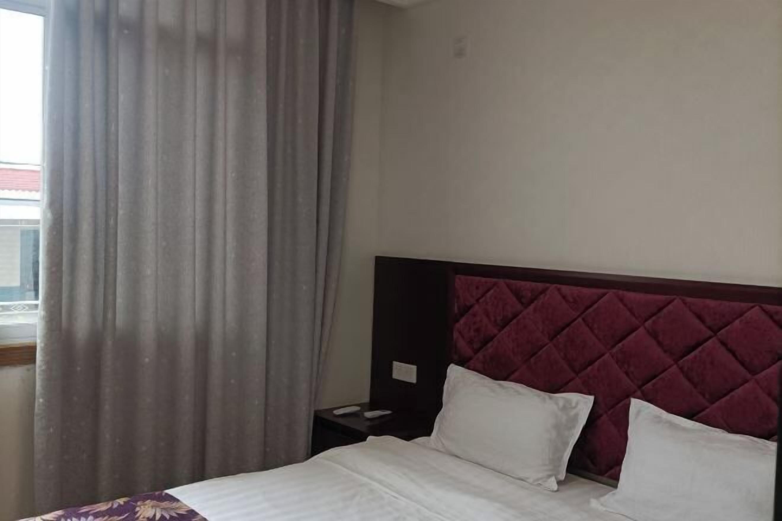 Une chambre d’hôtel avec un lit, une table de chevet, une fenêtre avec des rideaux et une vue sur un bâtiment à l’extérieur.