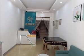 A hotel reception area with a reception desk, a staircase, and a seating area with a table. - Xiang Long Hotel (Guanghan)
