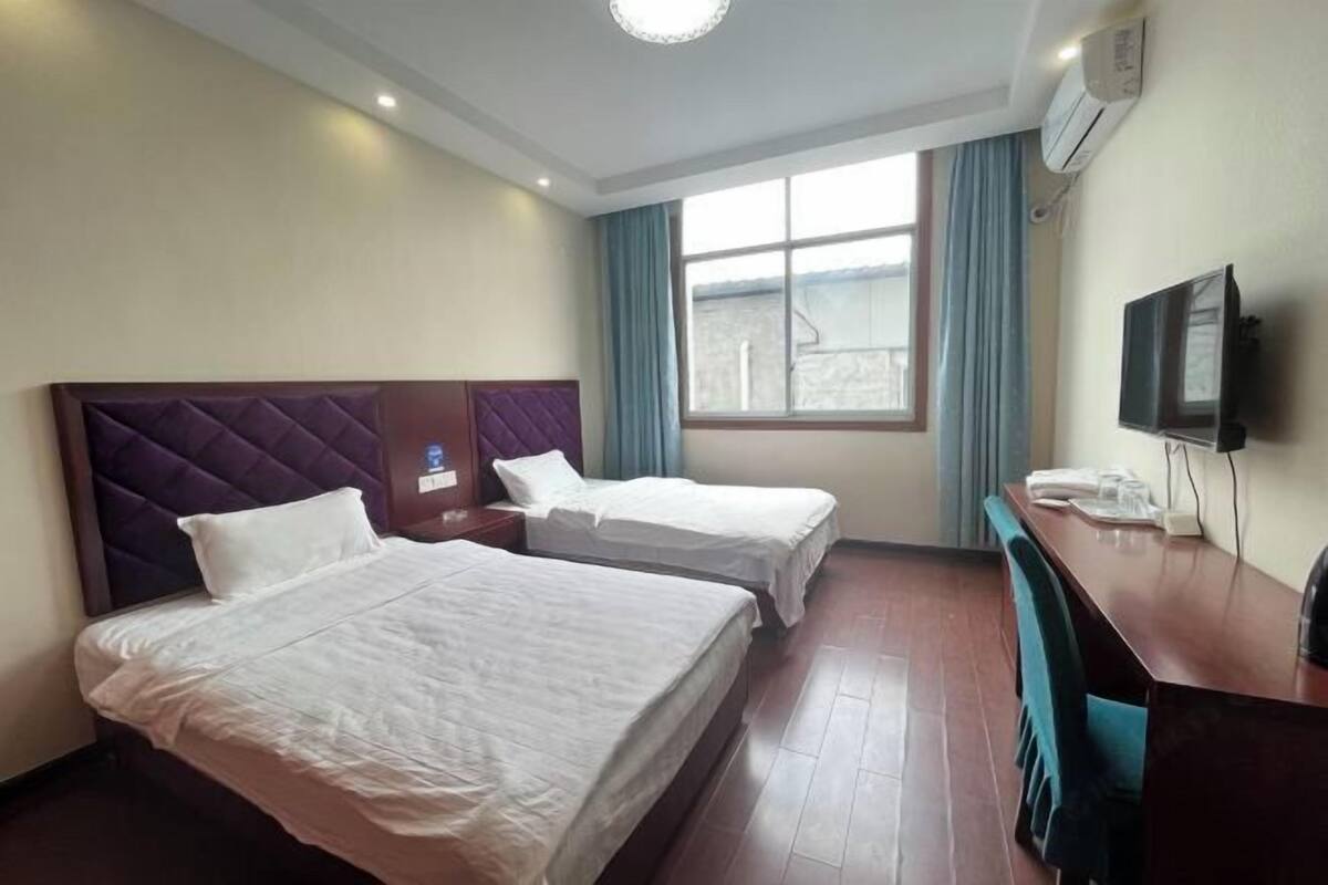 A hotel room with two beds, a desk, a television, and a window with curtains.