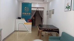 A hotel reception area with a blue banner, a reception desk, a staircase, a table, and a sofa. - Xiang Long Hotel (Guanghan)