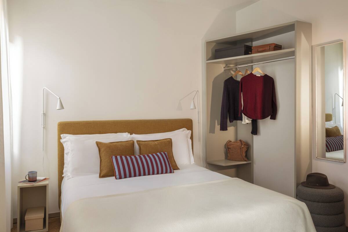 A neatly arranged hotel room with a bed, bedside lamps, a wardrobe, and a mirror.