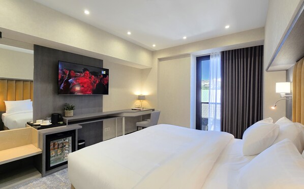 Une chambre d’hôtel avec un grand lit, un bureau avec une chaise, un téléviseur fixé au mur et une fenêtre avec des rideaux.