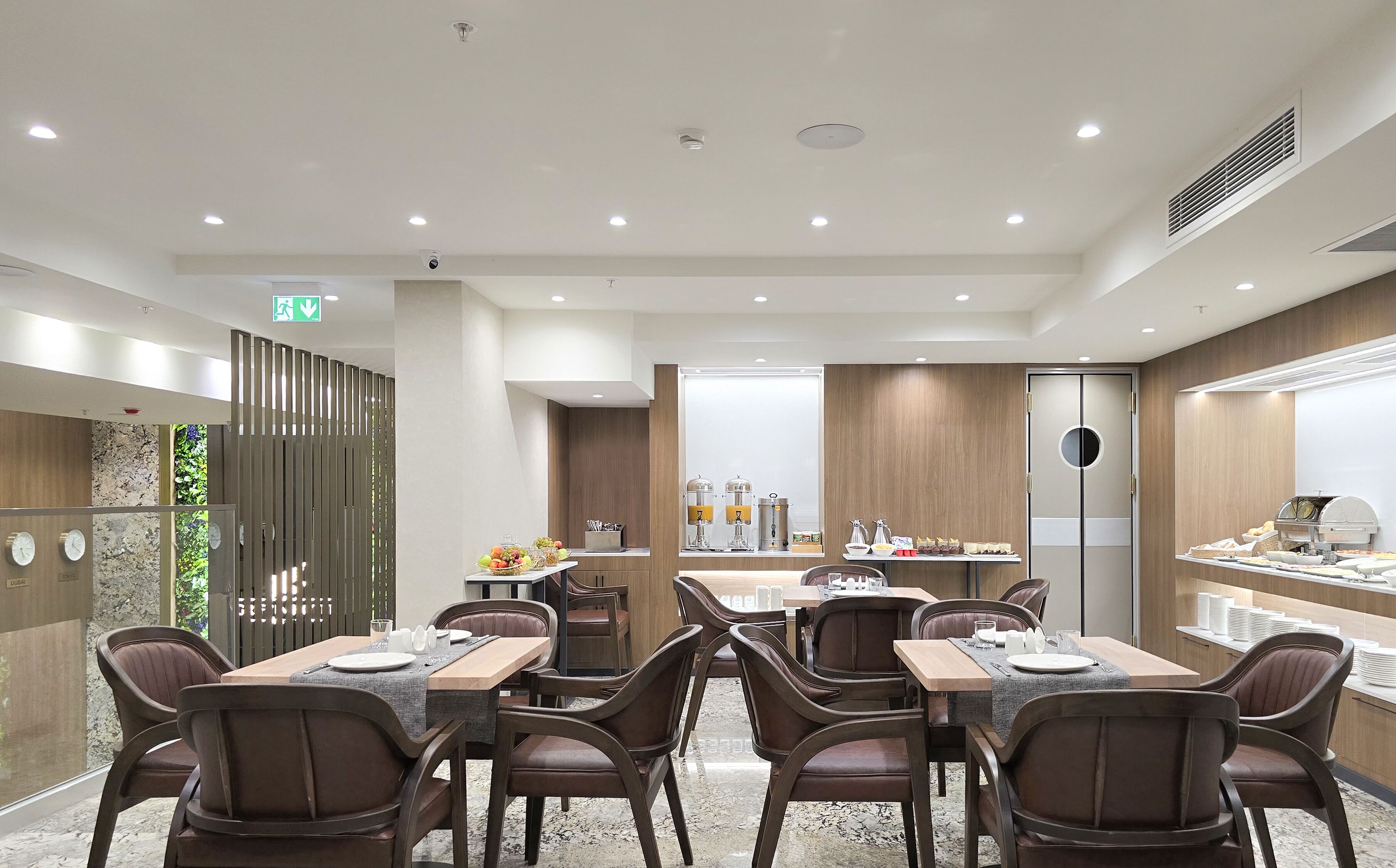 A modern dining area with multiple tables and chairs, equipped with coffee machines and a buffet.