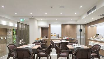 A modern dining area with multiple tables and chairs, equipped with coffee machines and a buffet.