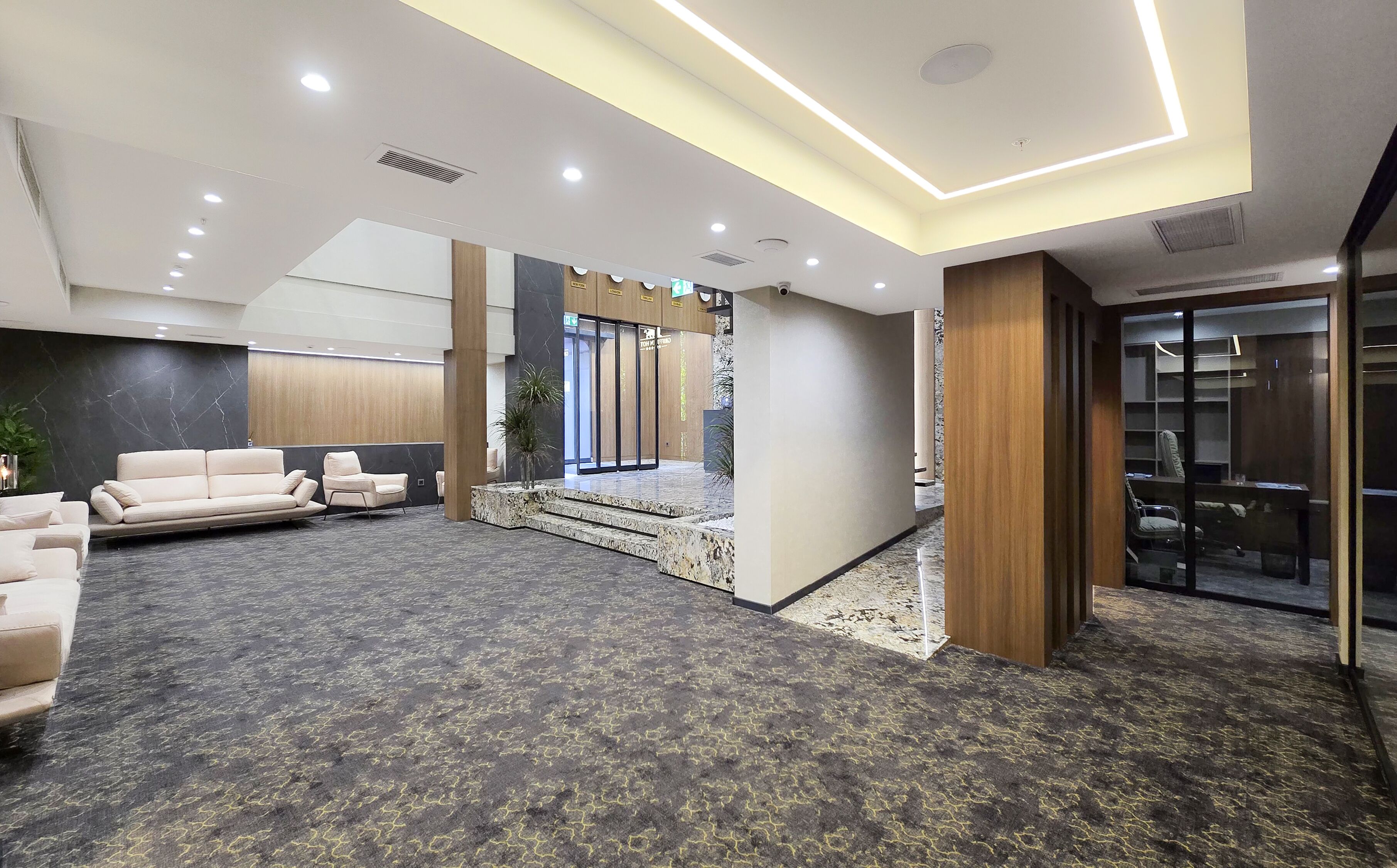 Un hall d’entrée spacieux avec un sol en marbre, un coin salon avec des canapés, un comptoir de réception et un escalier menant à un autre niveau.