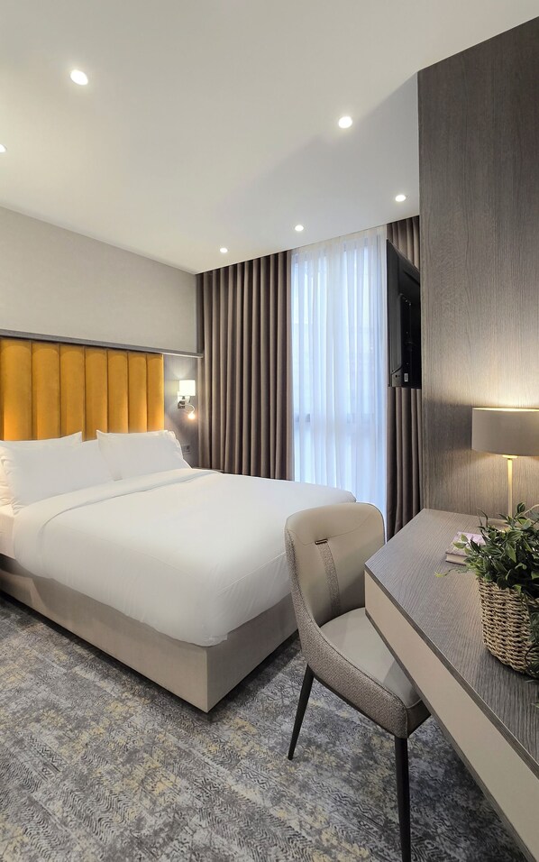 A modern hotel room with a large bed, a desk with a chair, a television, and a window with curtains. - Griffin Hotel (Tbilisi)