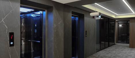 A modern interior with a marble floor, recessed lighting, and glass doors leading to an elevator.