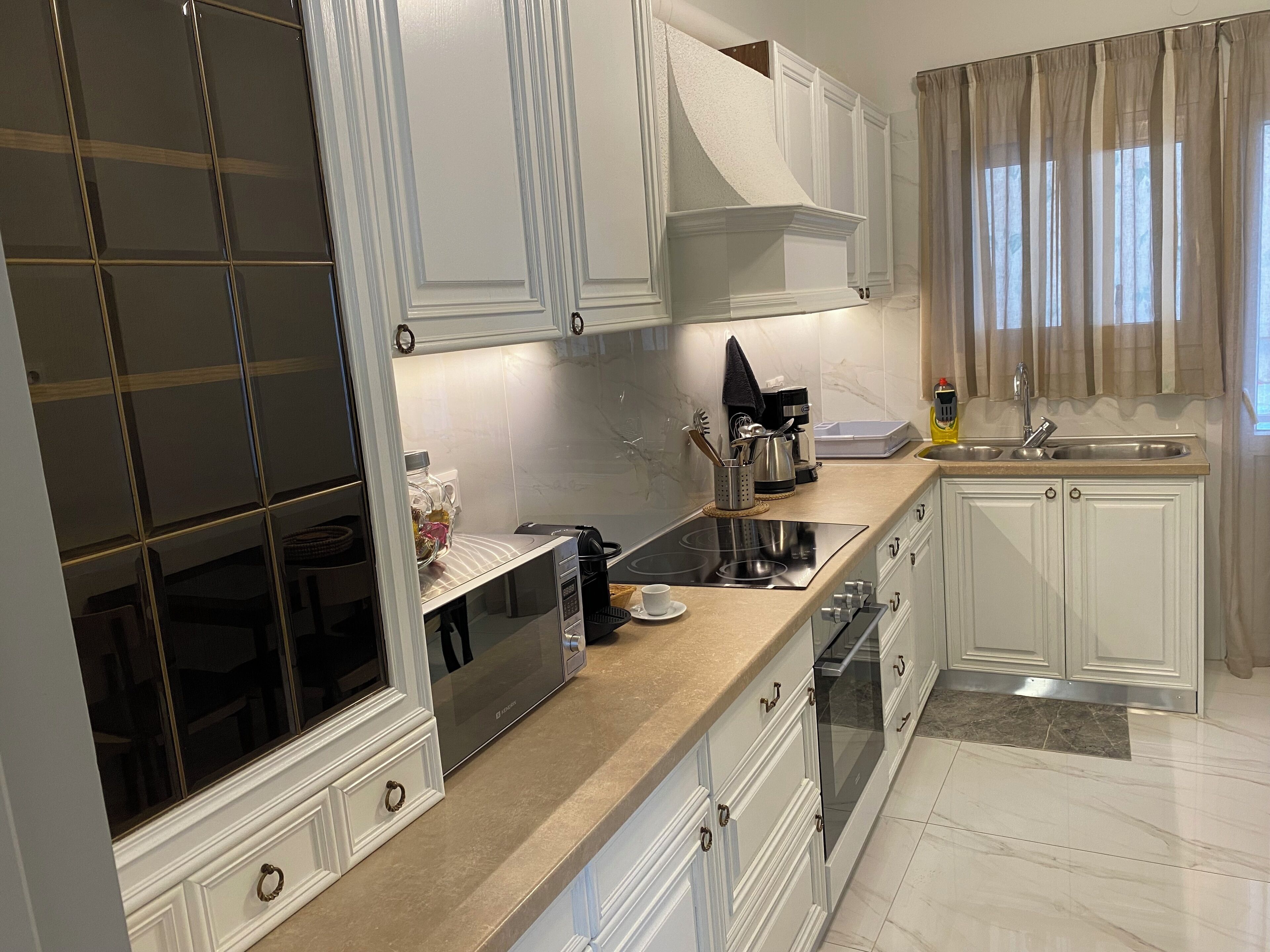 Une cuisine moderne avec des meubles blancs, une plaque de cuisson à induction noire, un four encastré et un évier en acier inoxydable.