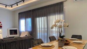 A modern dining area with a wooden table set for four, surrounded by chairs. A television is mounted on the wall to the left. - Angel's Apartment Volos (Volos)