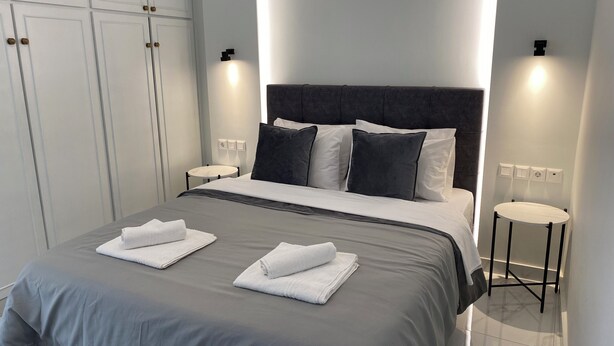 A modern hotel room with a large bed, two bedside tables, a wardrobe, and wall-mounted lighting. - Angel's Apartment Volos (Volos)