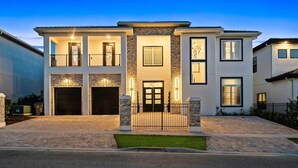 A modern two-story house with a stone facade, a front entrance with a black door, and a driveway leading to a garage. - Bear's Den At Reunion Resort-TB024 (Kissimmee)