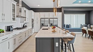 A modern kitchen with white cabinets, stainless steel appliances, and a central island with seating. - Bear's Den At Reunion Resort-TB024 (Kissimmee)