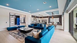 A spacious living room with a large blue sofa set, a coffee table, and a modern kitchen in the background. - Bear's Den At Reunion Resort-TB024 (Kissimmee)