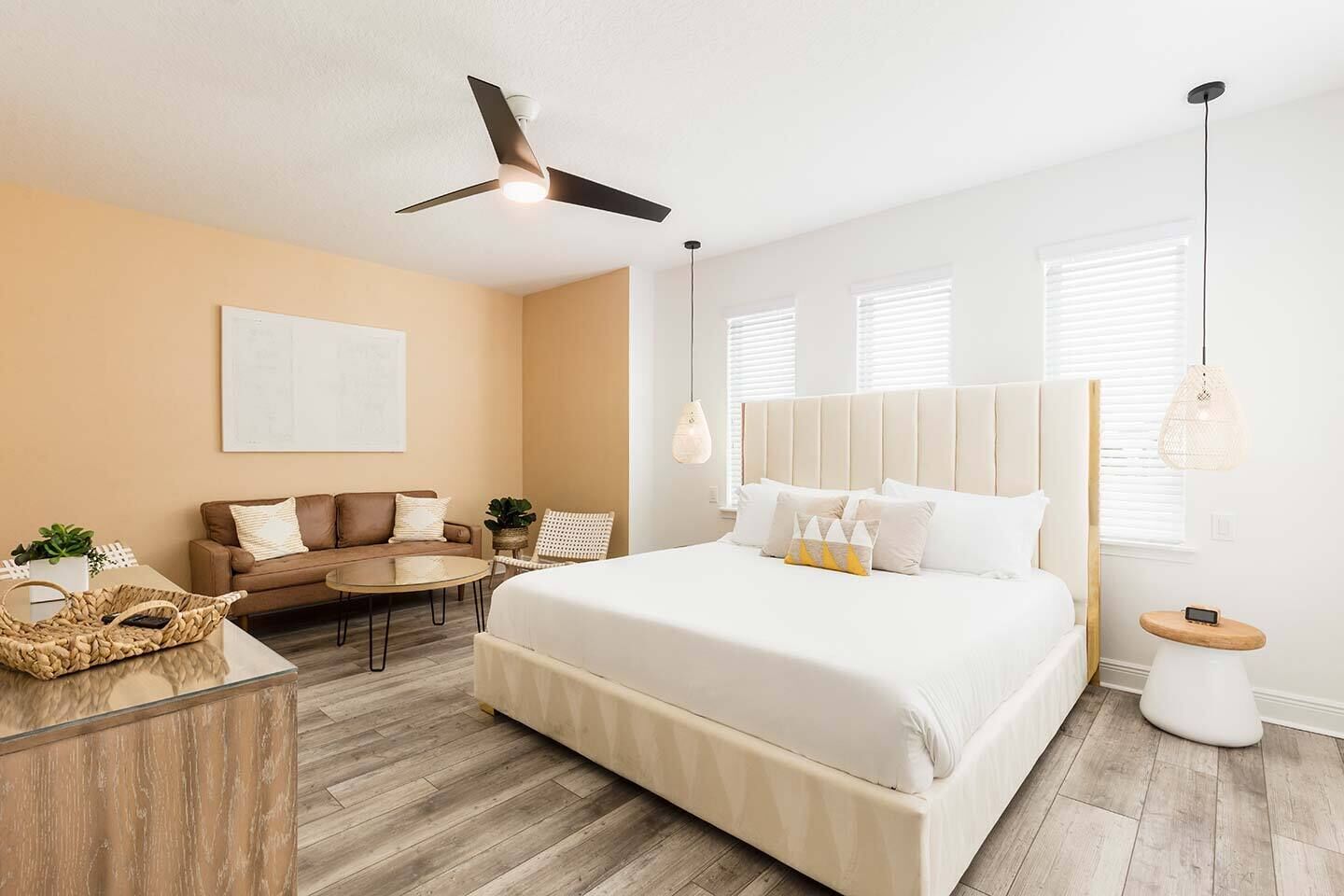 Une chambre à coucher moderne avec un grand lit, un ventilateur de plafond, un canapé, une table basse et une petite table d’appoint.