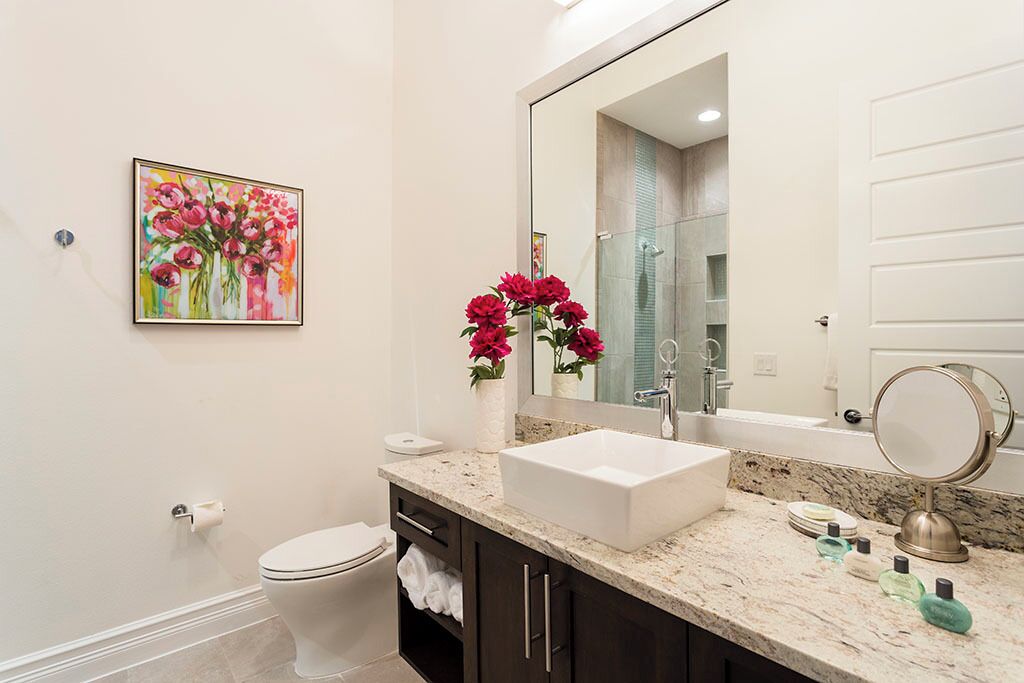 Une salle de bain avec un lavabo blanc, des meubles sombres, un grand miroir et un tableau représentant des fleurs accroché au mur.