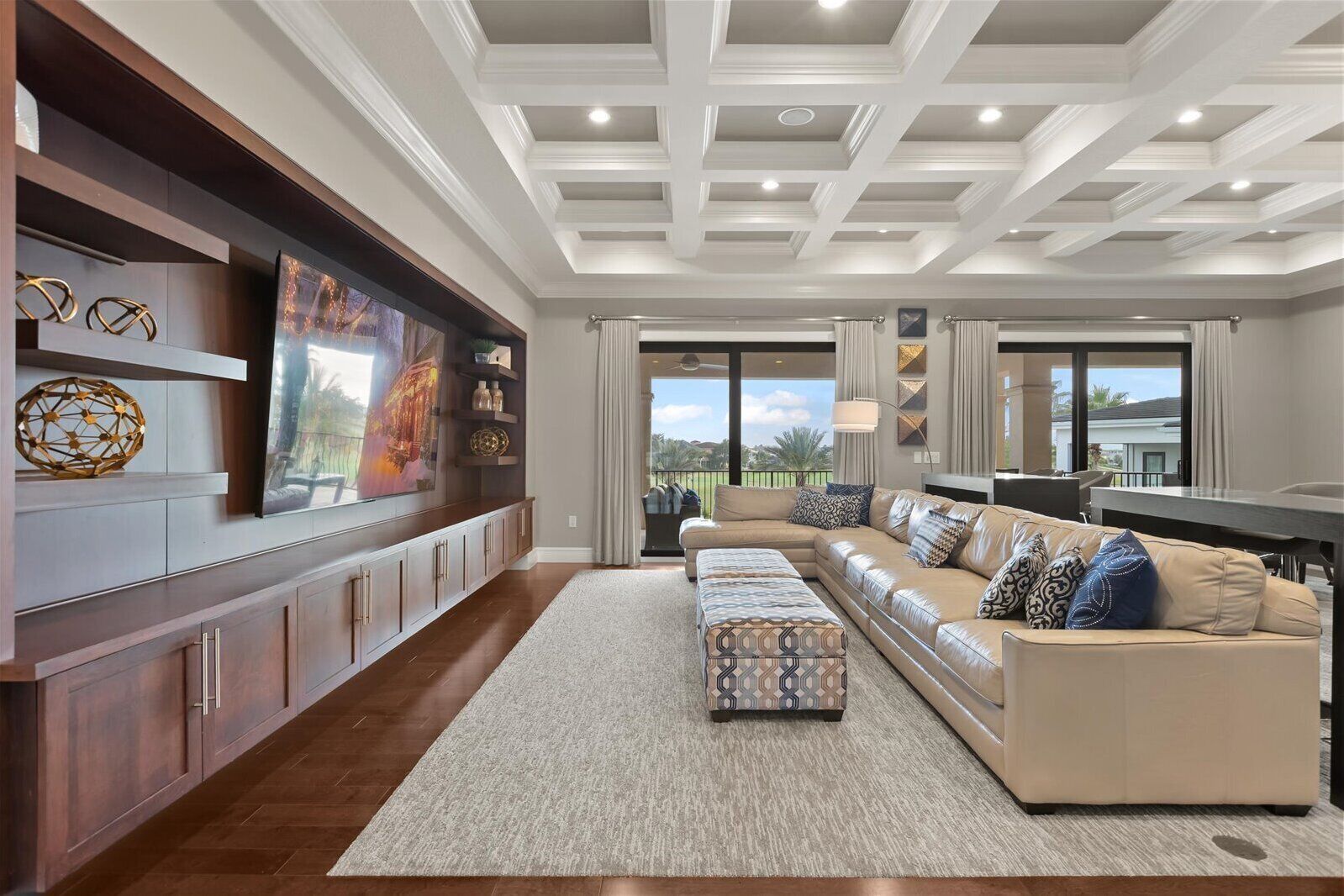 A spacious living room with a large sectional sofa, a coffee table, and a TV mounted on the wall.