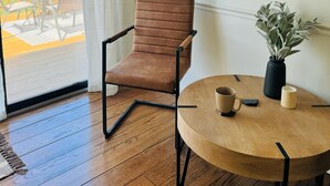 Una habitació amb una cadira marró, una taula rodona de fusta amb un ram i dues tasses, un quadre amb marc i un mirall a la paret.