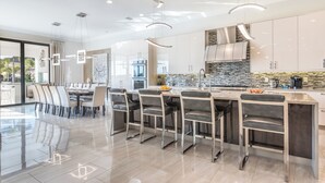 A modern kitchen with a central island, stainless steel appliances, and a large window overlooking a pool. - The Superhero Haven-TT276 (Kissimmee)