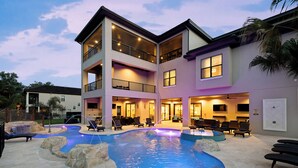 A multi-story hotel with a swimming pool, outdoor seating, and a well-lit lobby.