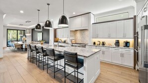 A modern kitchen with white cabinets, a large island with bar stools, and stainless steel appliances.