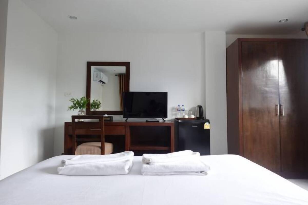 A hotel room with a bed, a desk with a television, a wardrobe, and a small cabinet.